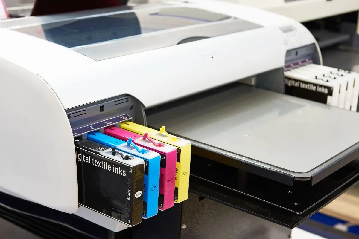Close-up of a digital printer loaded with CMYK ink cartridges, representing colour management and printing accuracy from screen to print.