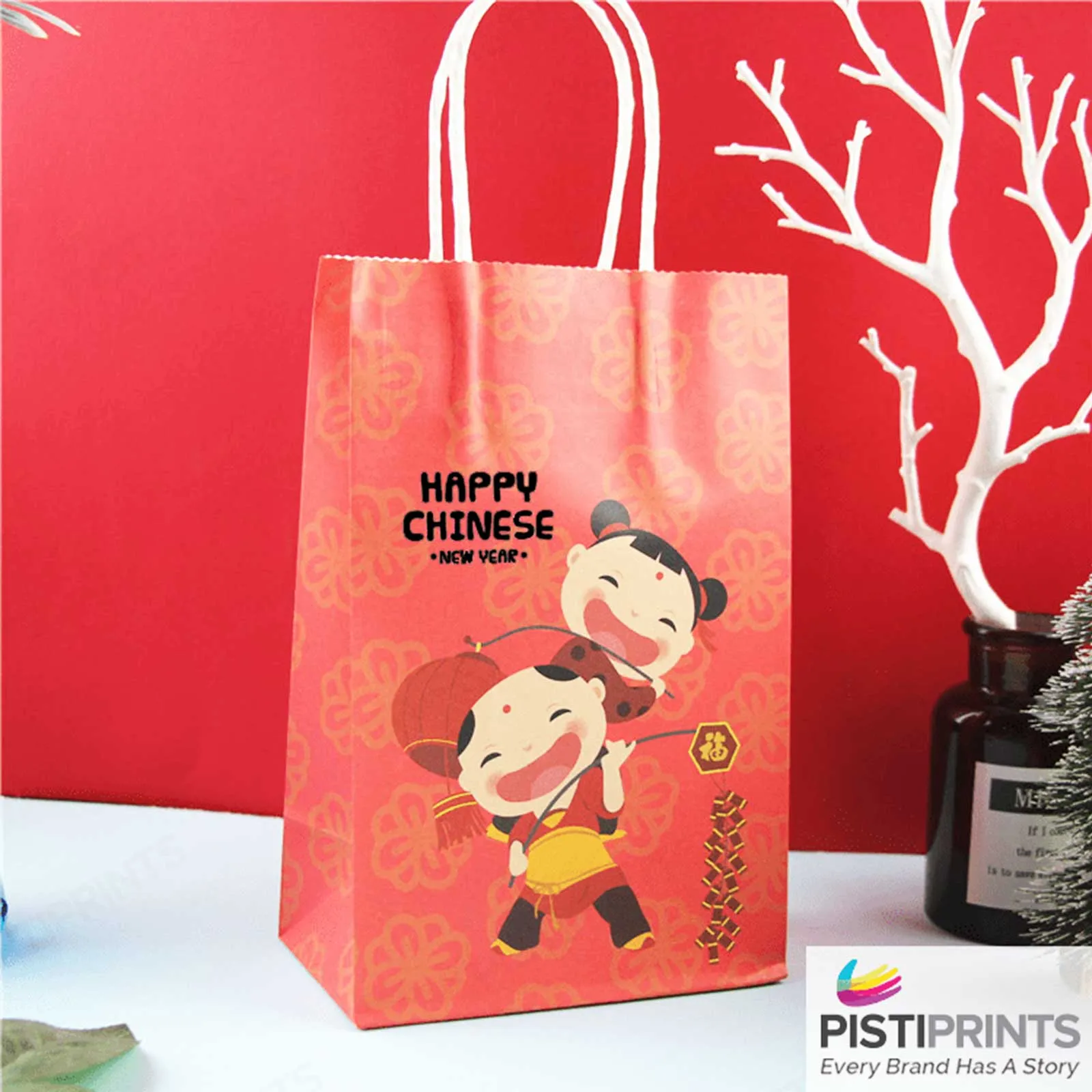Red Chinese New Year gift bag with cartoon children illustration and the text “Happy Chinese New Year,” displayed on a white surface with decorative elements in the background.